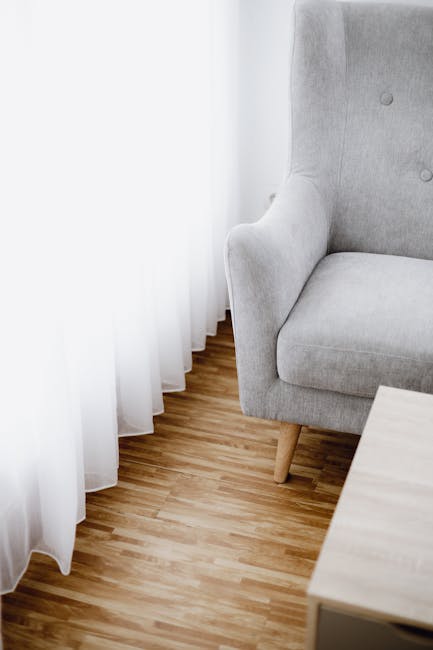 Close-up view of a grey upholstered sofa with matching cushions in a living room setting. The fabric surface appears clean and well-maintained, with no visible dust or stains. The sofa is positioned a